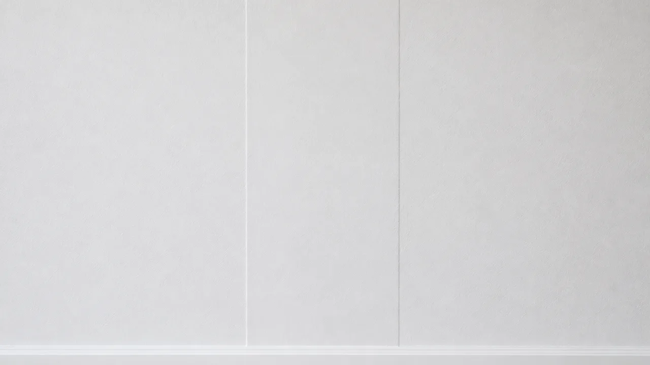 Mur intérieur peint en blanc sur lequel un joint de plaques de plâtre non ratissé se devine en lumière rasante, révélé par une fine ligne claire sur son bord gauche et une fine ligne sombre sur son bord droit